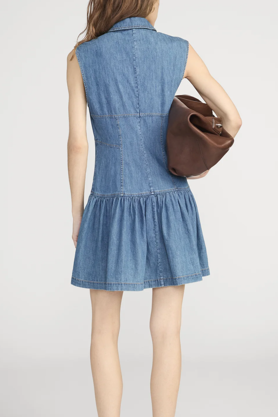 women wearing a sleeveless collared denim dress with a brown bag 