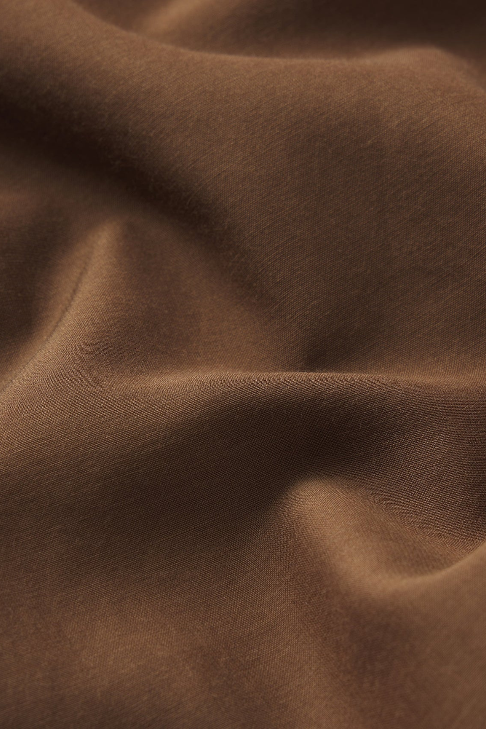 A close-up of draped brown fabric with soft folds and a smooth texture.