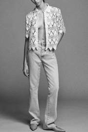 Person wearing a floral lace top and jeans on a gray background