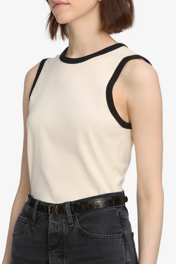 Woman wearing a cream sleeveless top with black trim and dark jeans on a white background
