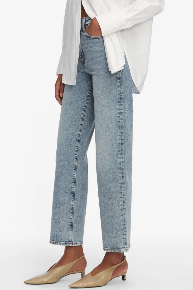 Person wearing light blue jeans and a white top on a plain background
