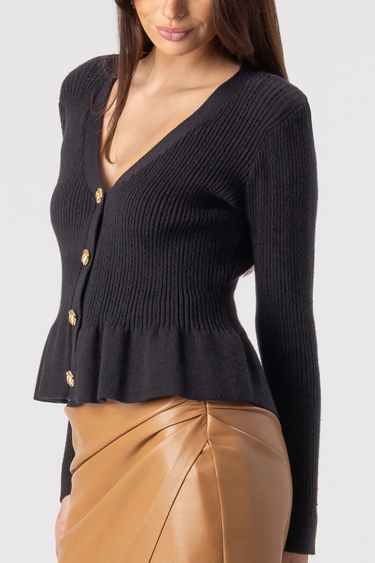 Black ribbed cardigan with gold buttons worn by a person, on a white background