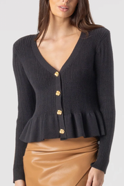 Black ribbed cardigan with gold buttons worn by a model on a white background