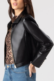 Person wearing a black leather jacket over a leopard print top with blue jeans on a light gray background