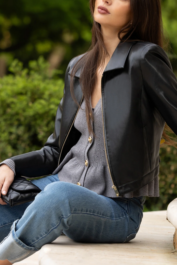 Woman wearing a black leather jacket and blue jeans sitting outdoors.