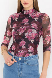 Woman wearing a floral mesh bodysuit with a plain background