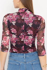 Woman wearing a floral long-sleeve top with sheer panels and blue jeans on a white background