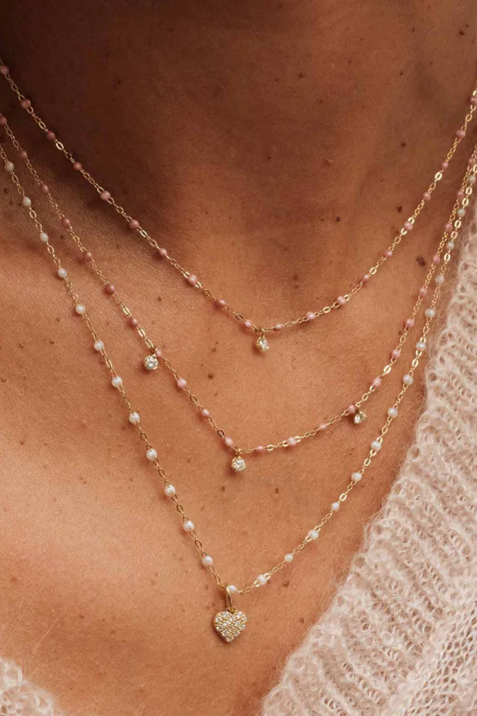 Close-up of a person wearing multiple necklaces with heart pendants.