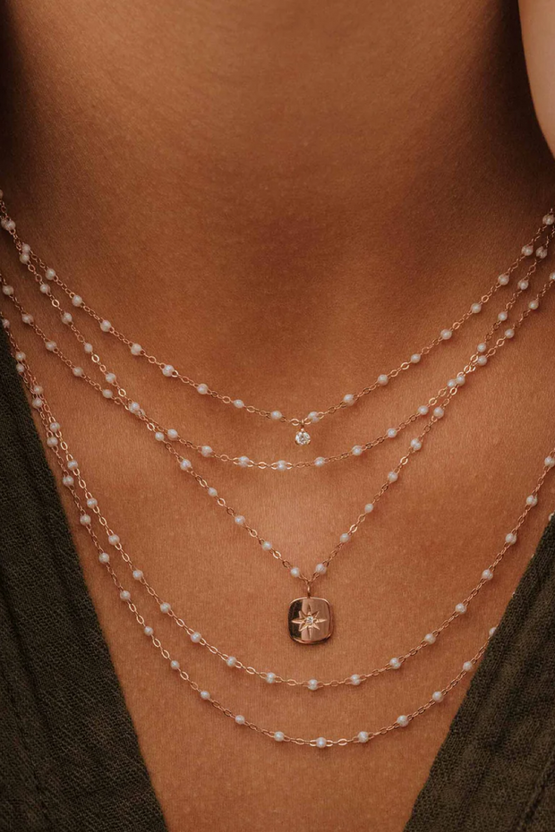 Close-up of a person wearing multiple opal and gold necklaces with a pendant.