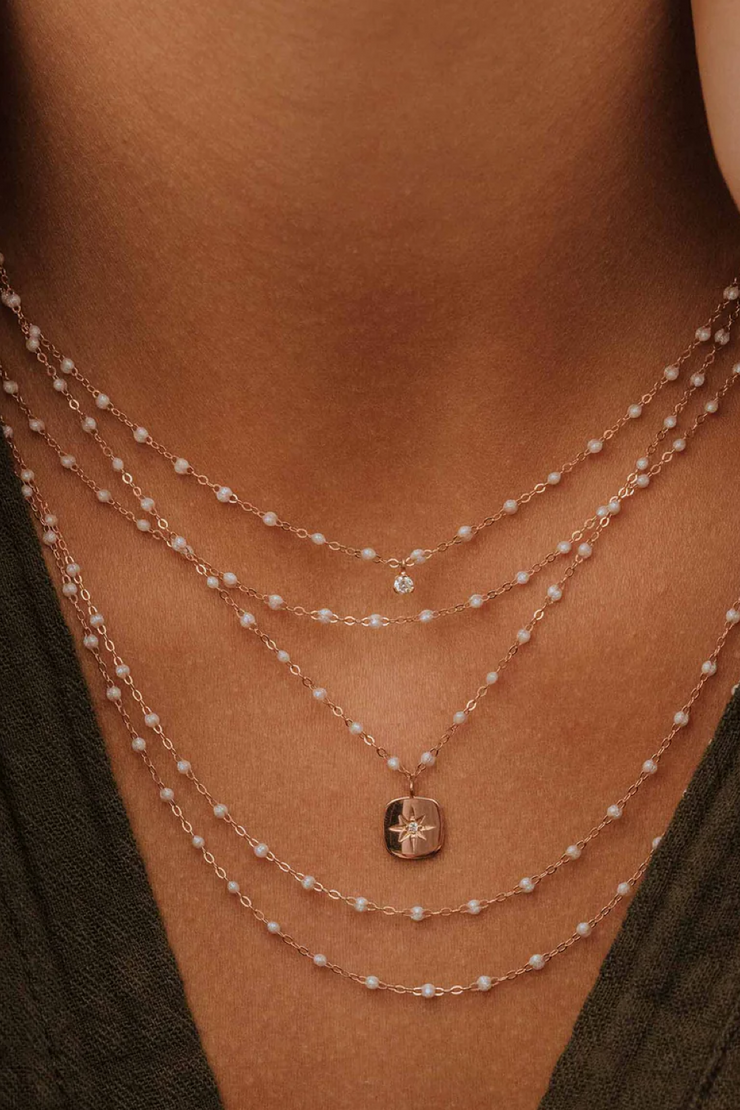 Close-up of a person wearing multiple opal and gold necklaces with a pendant.