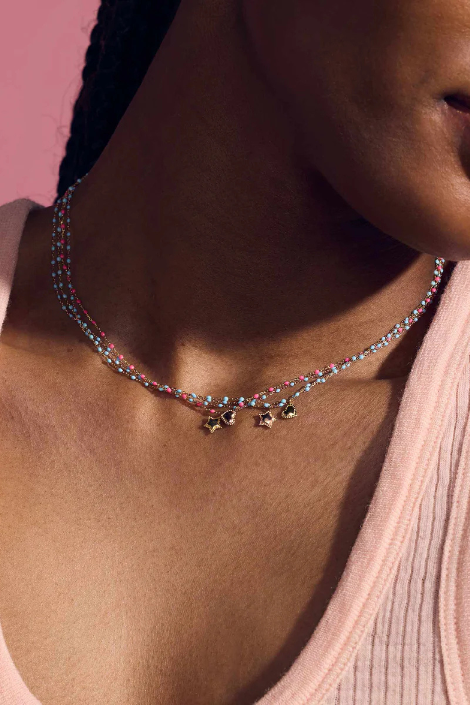 Necklace with heart pendants on a person against a pink background