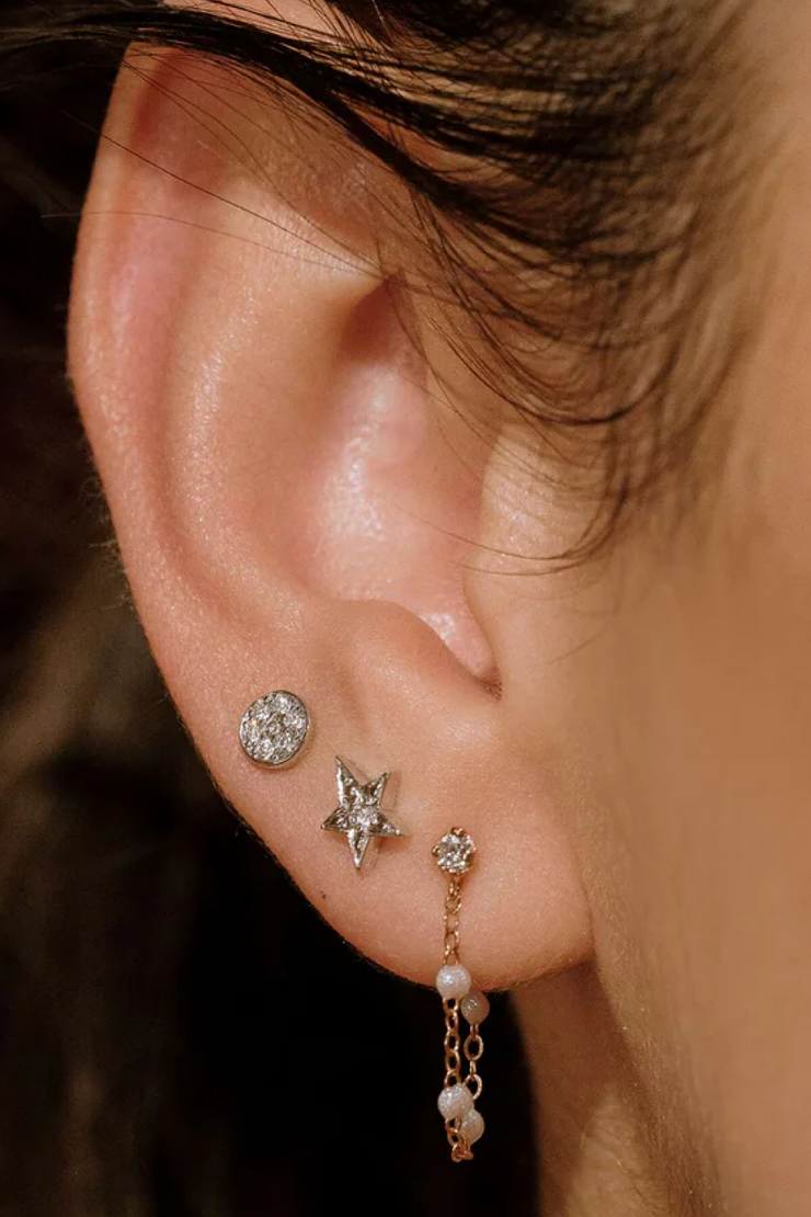 Close-up of an ear with three earrings: a star-shaped earring, a round earring, and a dangling earring with pearls.