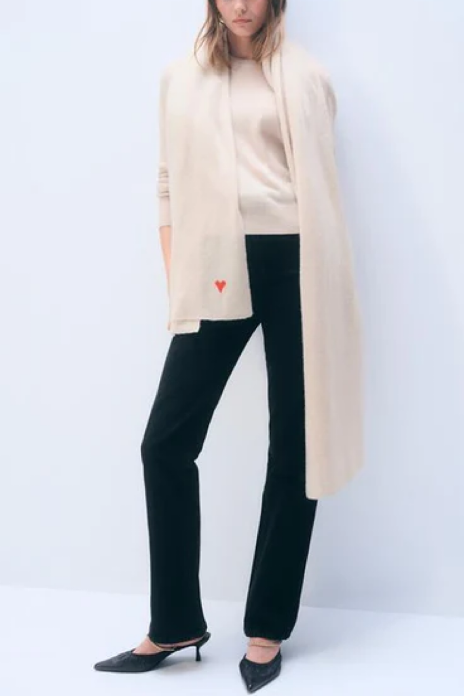 Person wearing a beige scraf, black pants, and black shoes on a white background