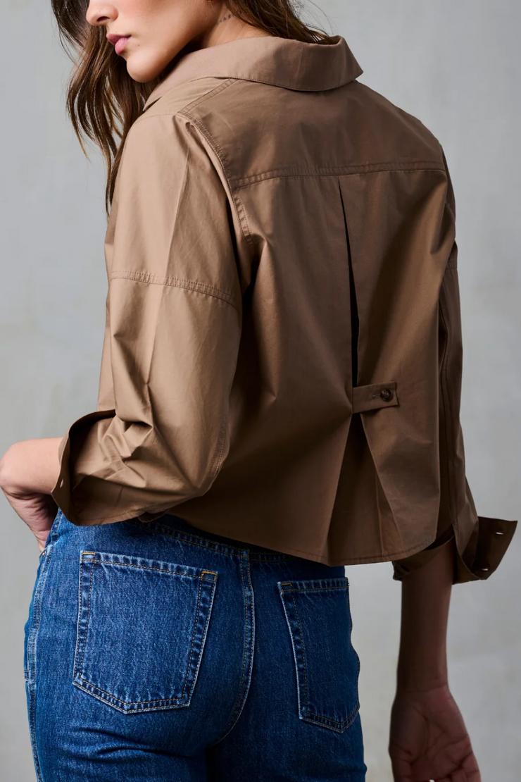 Person wearing a brown blouse and blue jeans against a gray background