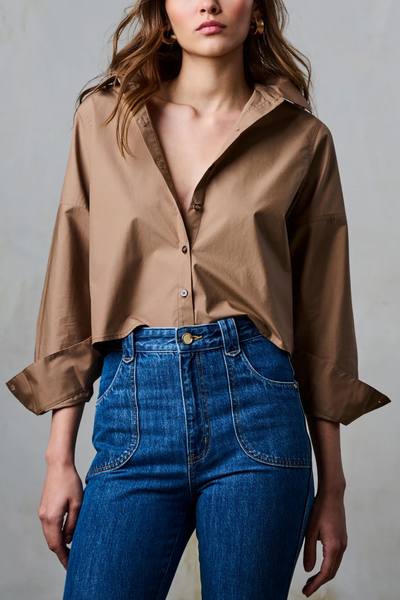 Woman wearing a brown blouse and blue jeans against a gray background