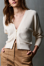 Woman wearing a ivory cardigan with brown pants against a gray background