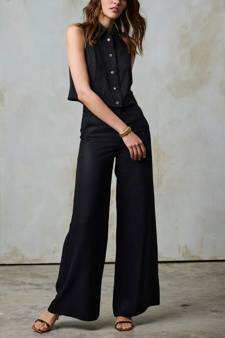 Woman wearing a black sleeveless top and pants against a textured wall.