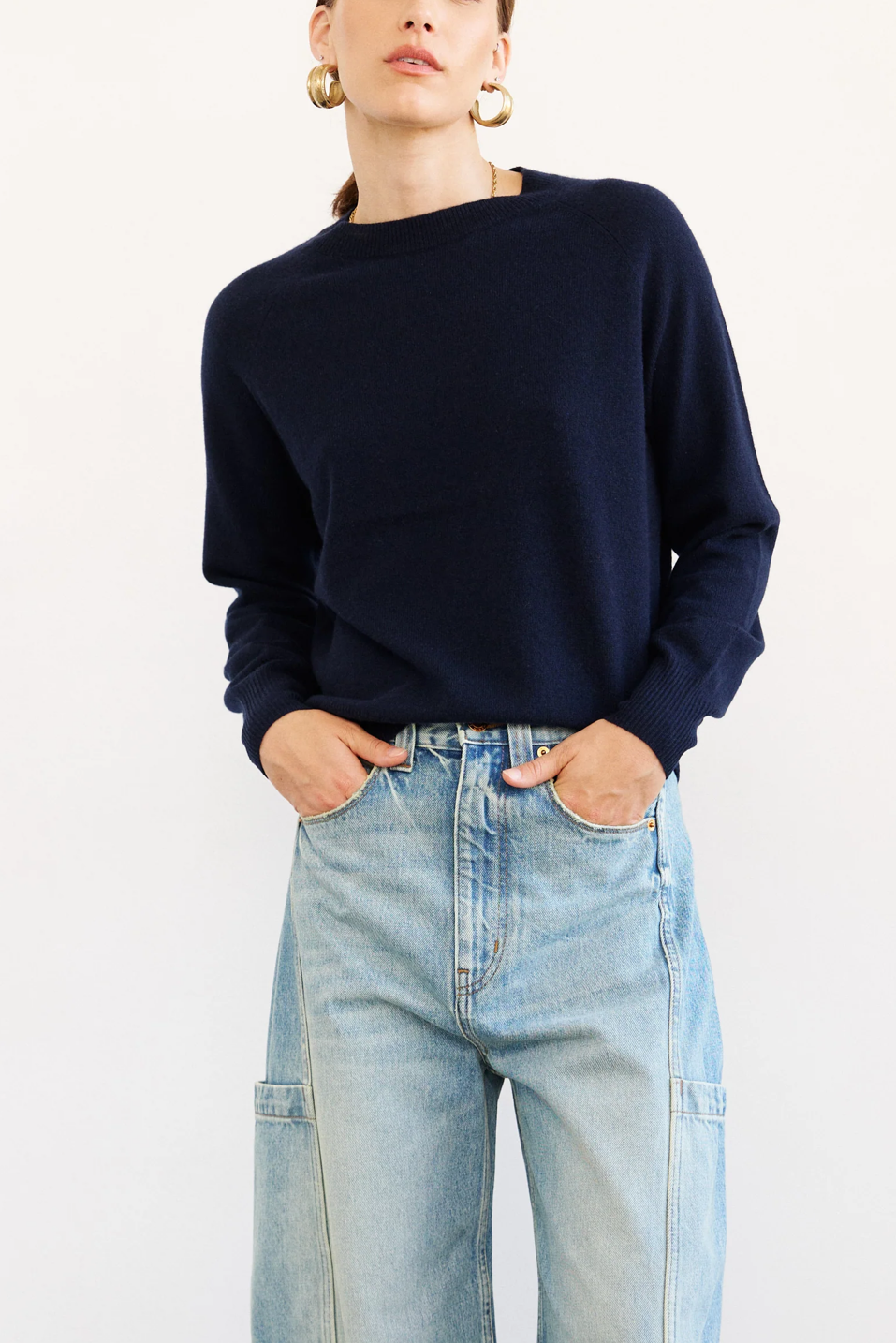 Person wearing a navy sweater and light blue jeans on a white background