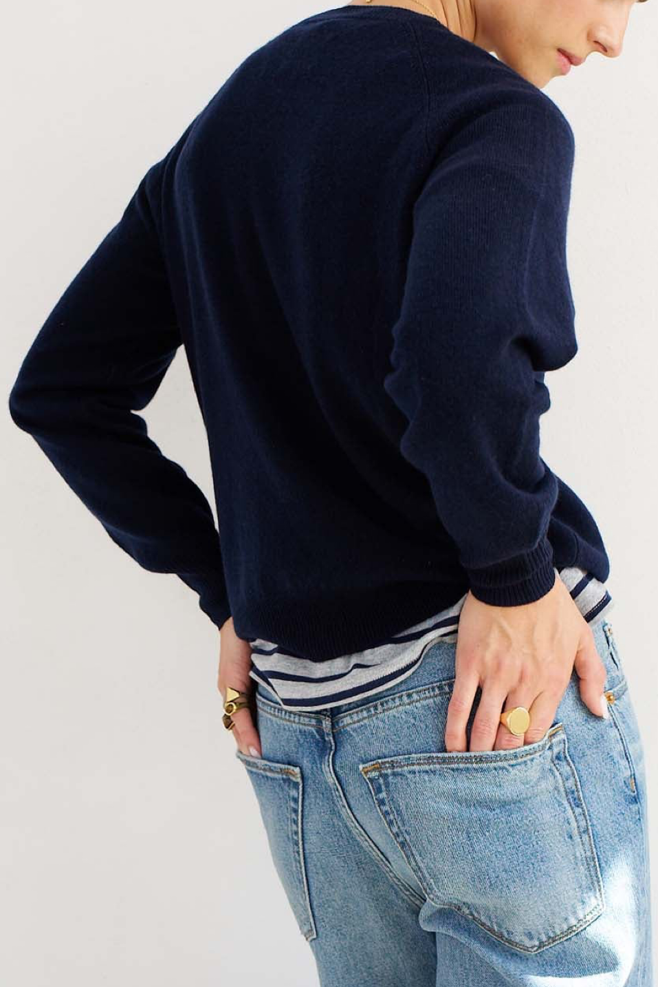 Person wearing a navy sweater and blue jeans on a light gray background