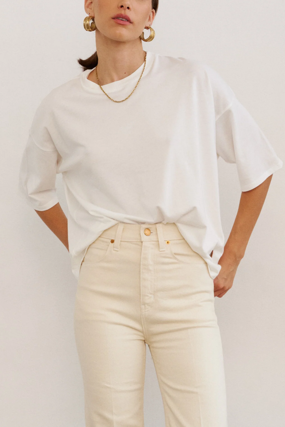 Person wearing a white oversized shirt and beige pants against a plain background