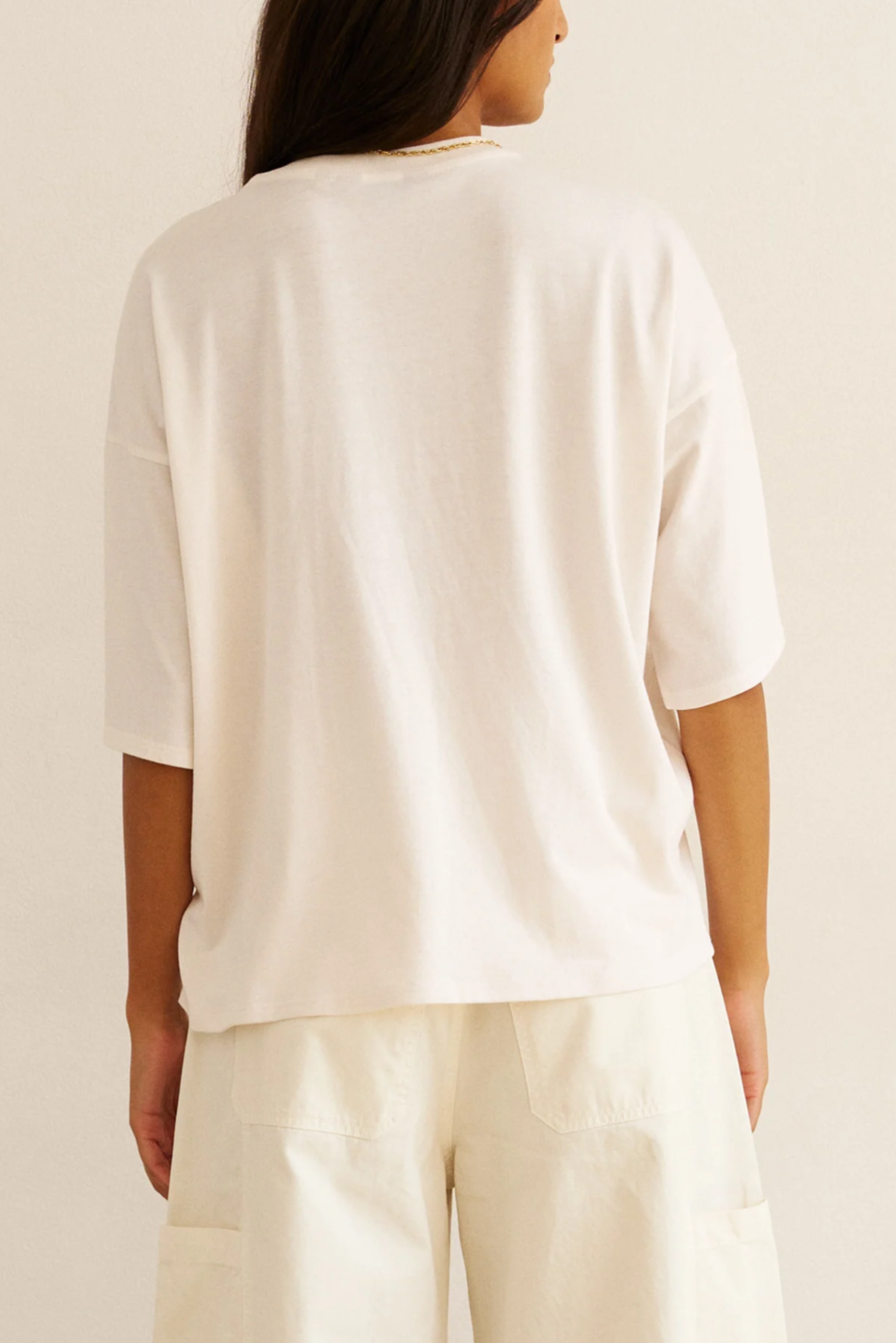 Person wearing a white top and beige pants on a plain background