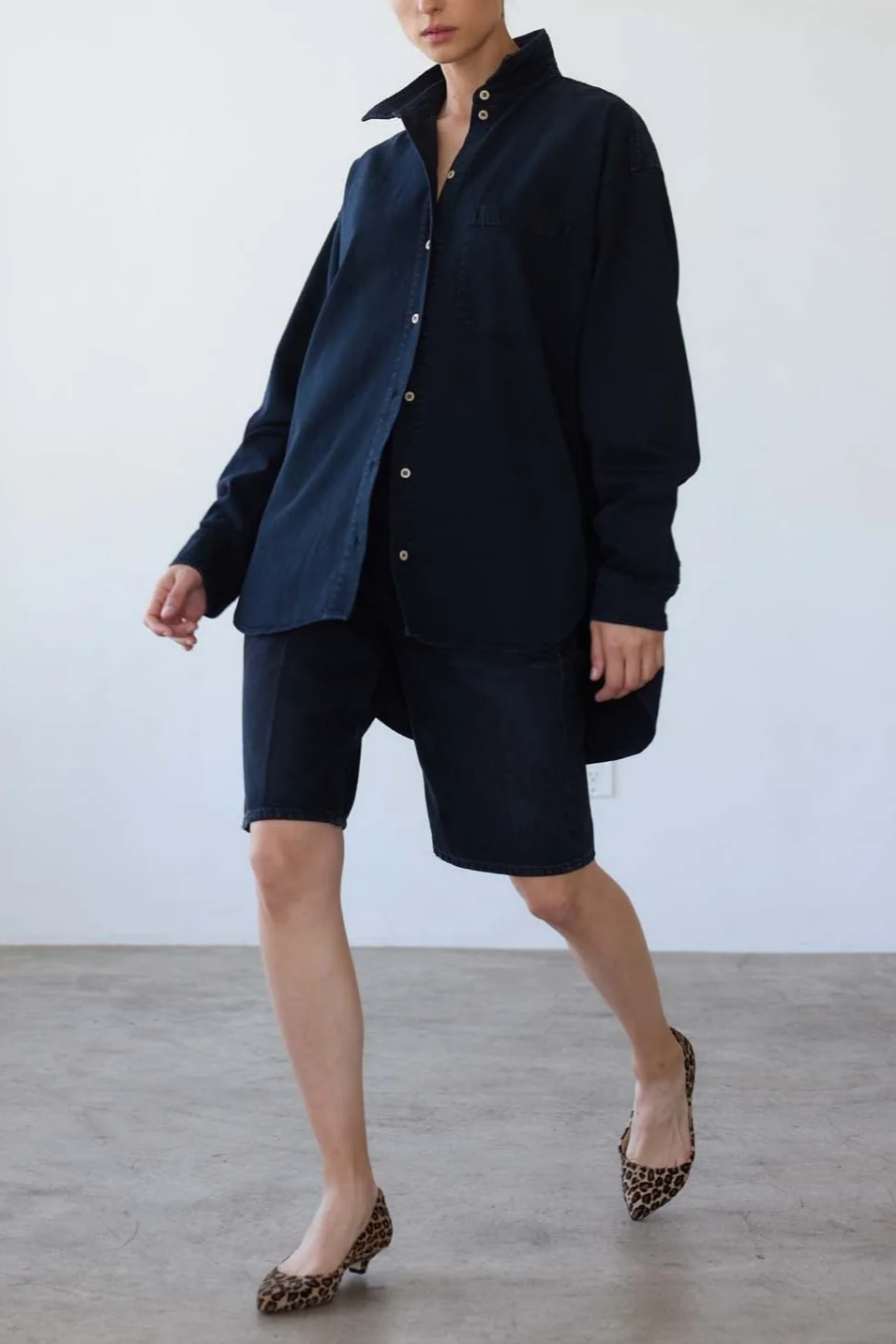 Person wearing a navy outfit with shorts and a button-up shirt against a white background