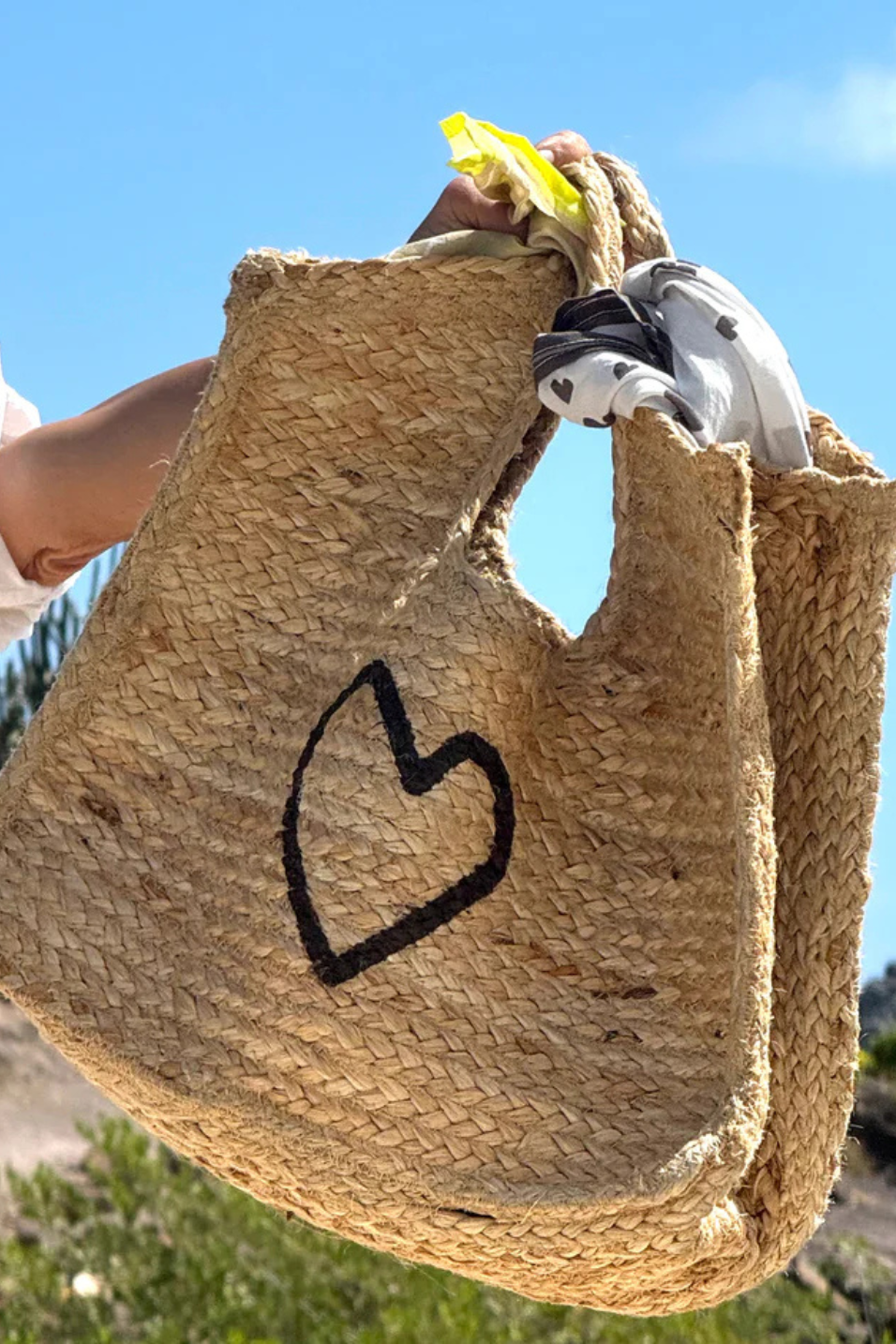 Woven bag with a heart design held against a blue sky.