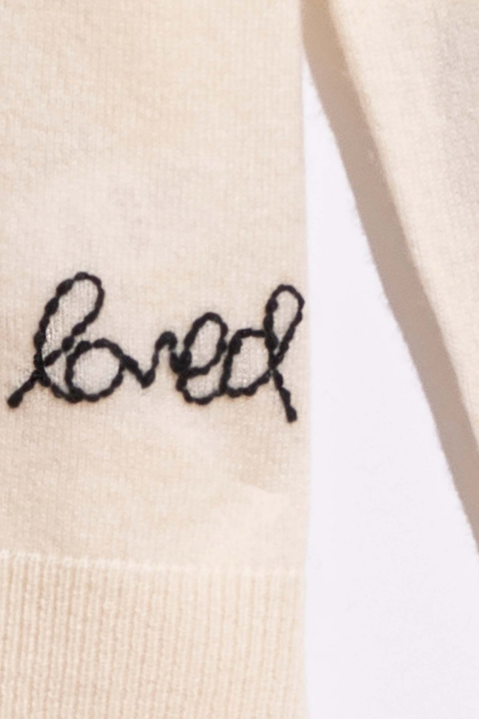 Textile with 'loved' embroidered in black on cashmere fabric.