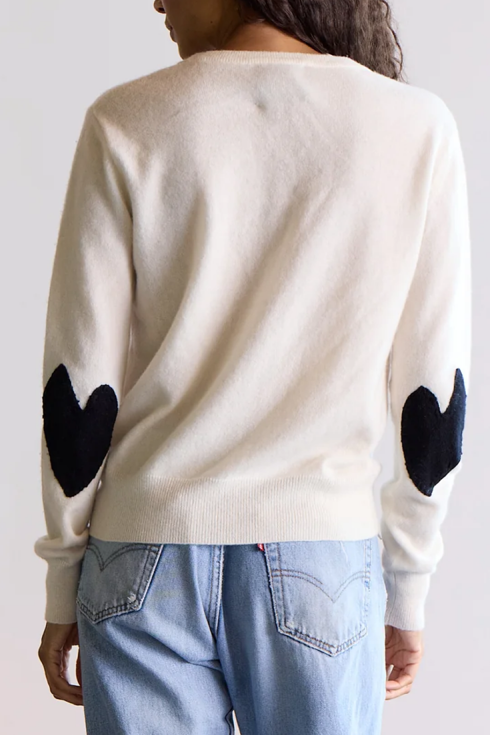 Person wearing a cream sweater with black heart designs on the sleeves against a white background