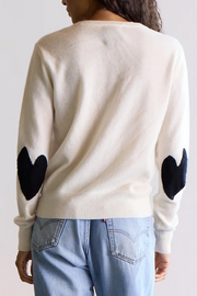 Person wearing a cream sweater with black heart designs on the sleeves against a white background