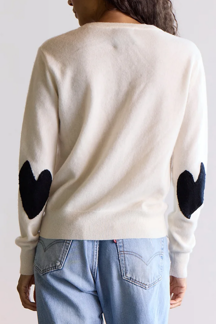 Person wearing a cream sweater with black heart designs on the sleeves against a white background
