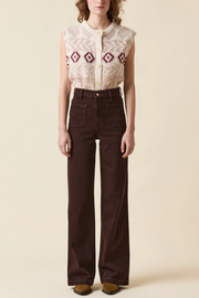 Person wearing a patterned sleeveless top and brown pants on a beige background