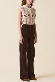 Person wearing a sleeveless patterned top and brown pants on a beige background