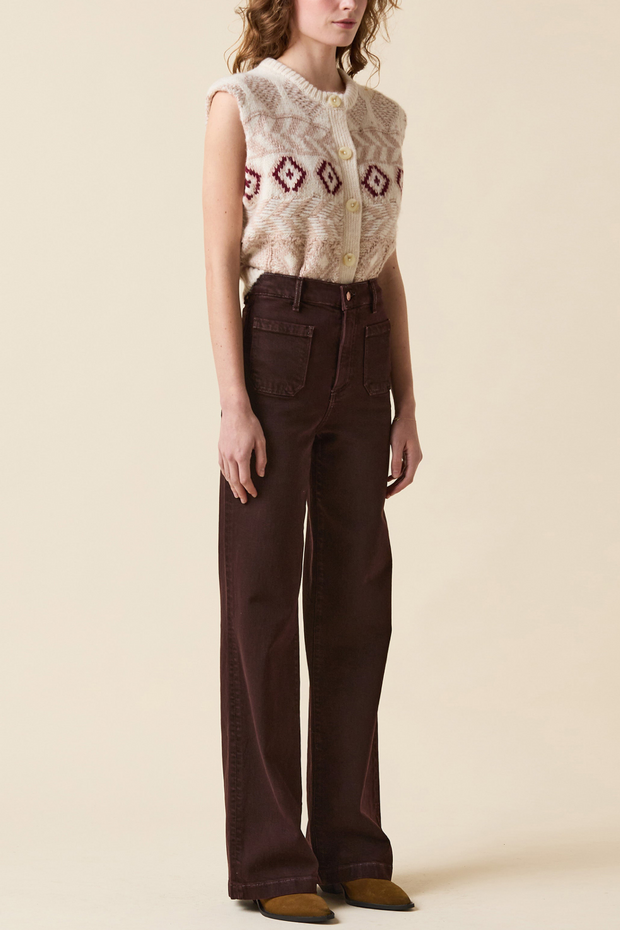 Person wearing a sleeveless patterned top and brown pants on a beige background