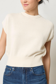 Person wearing a cream-colored sweater and blue jeans against a plain background