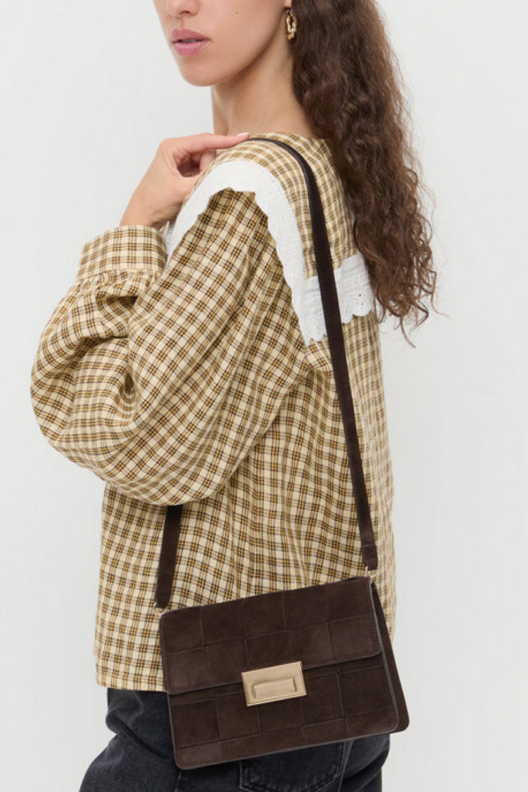 Woman wearing a plaid jacket with a brown handbag on a white background