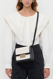 Woman wearing a white blouse with ruffled details and a black and white handbag.
