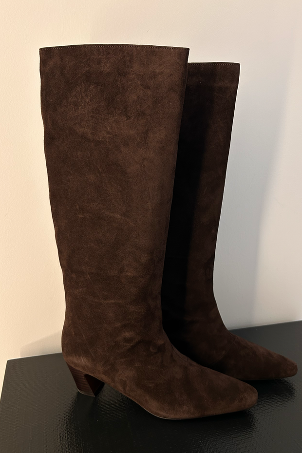 Pair of suede brown knee-high boots on a black surface with a white background