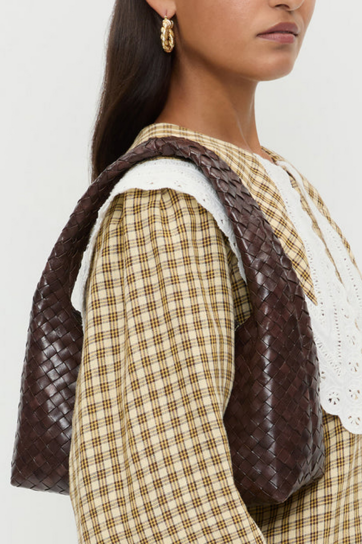 Woman wearing a plaid outfit with a brown woven bag over her shoulder against a white background