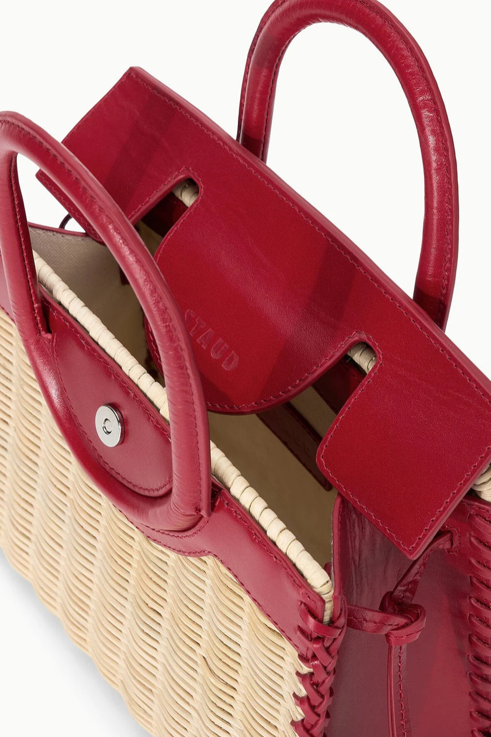 Close-up of a woven handbag with red leather handles on a white background