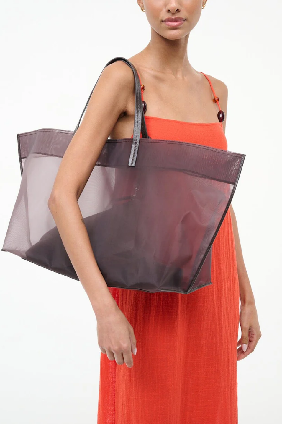 Woman wearing an orange dress holding a brown sheer tote bag on a white background