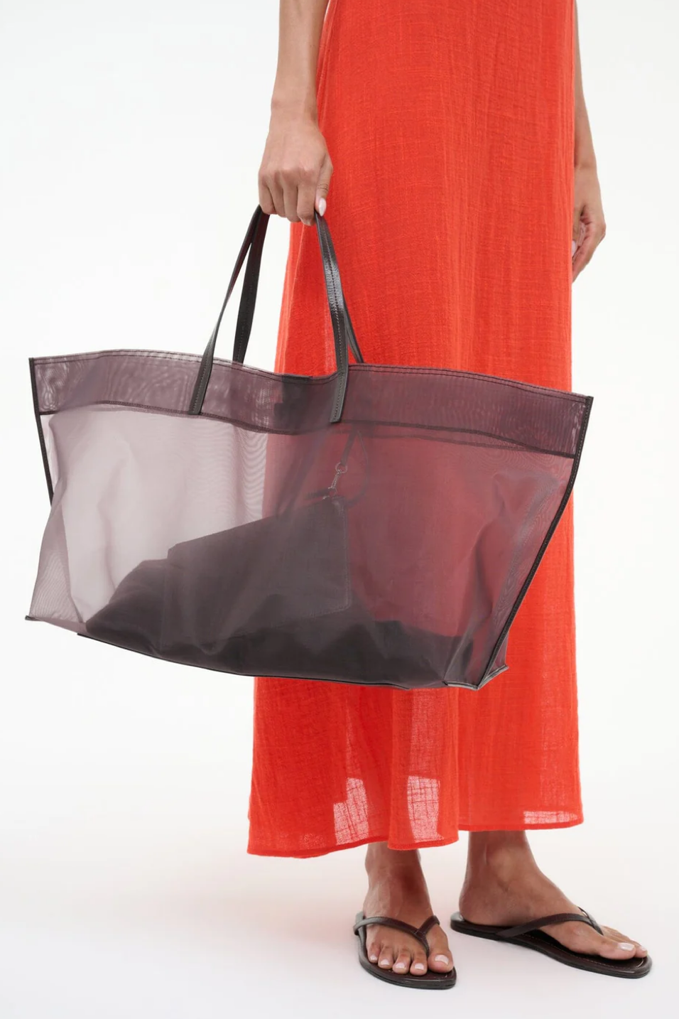 Person wearing an orange dress holding a brown mesh tote bag on a white background