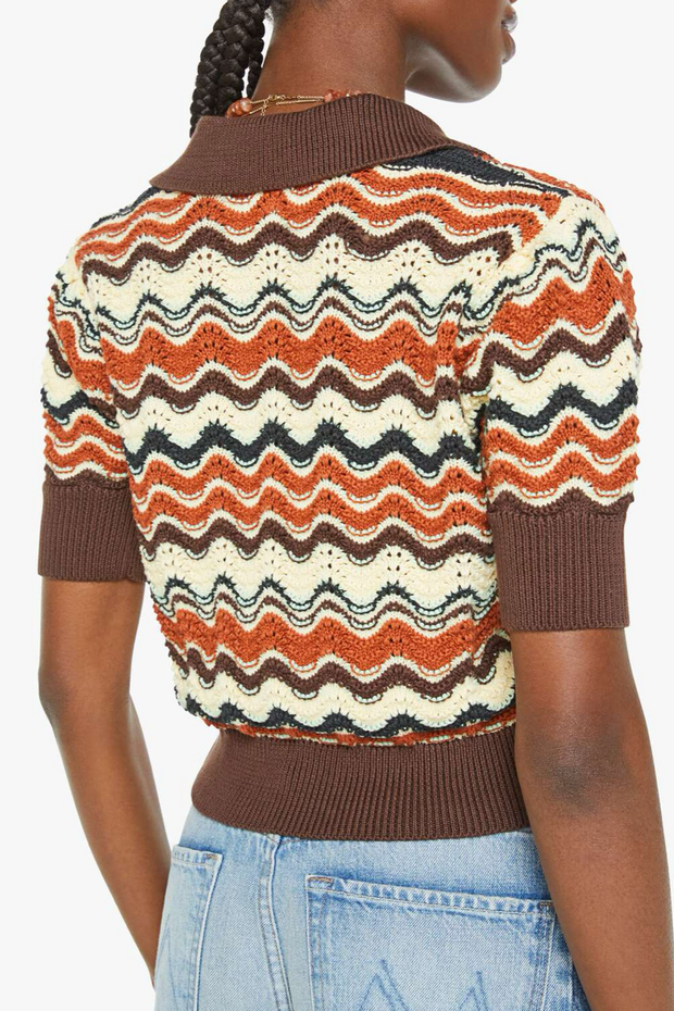 Person wearing a patterned sweater with wavy design and brown collar, paired with light blue jeans.