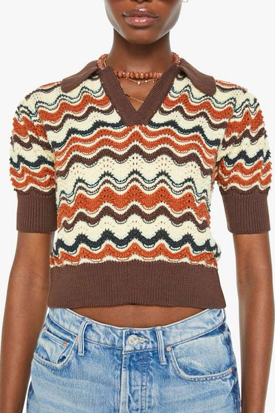 Person wearing a patterned sweater with short sleeves and jeans on a white background