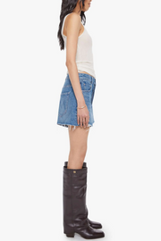 Woman wearing a white tank top, blue denim skirt, and black knee-high boots on a white background
