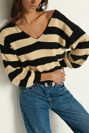 Person wearing a black and beige striped sweater with blue jeans against a white background