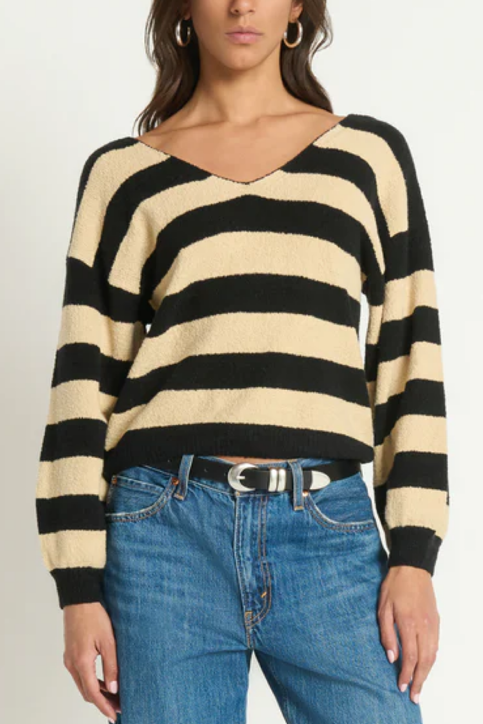 Person wearing a black and beige striped sweater with blue jeans on a plain background