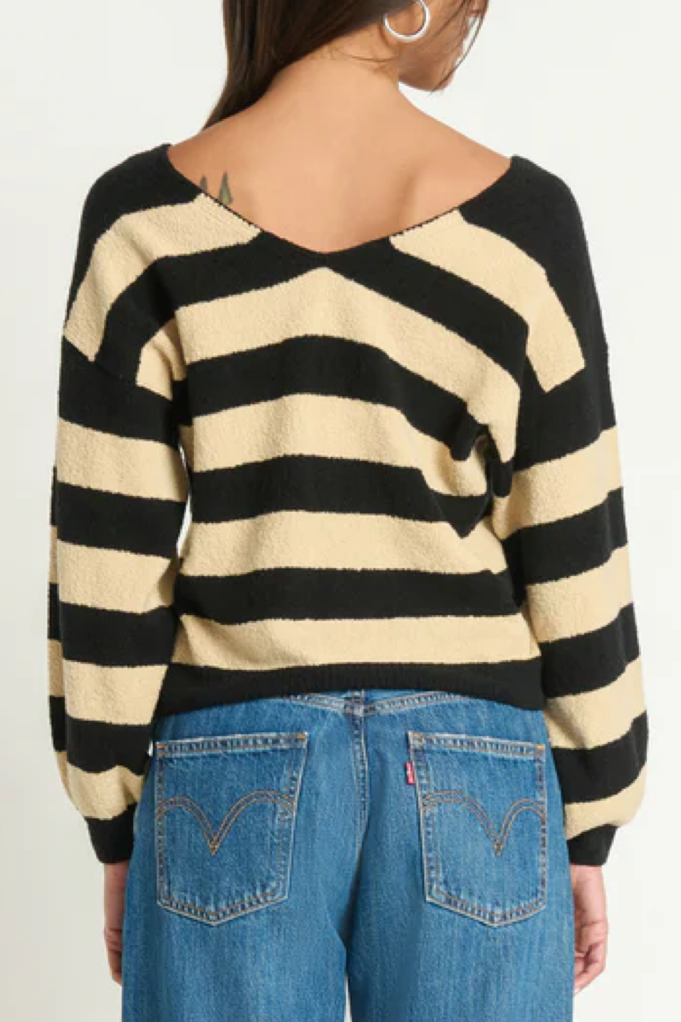 Person wearing a black and beige striped sweater with blue jeans