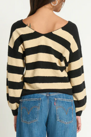 Person wearing a black and beige striped sweater with blue jeans