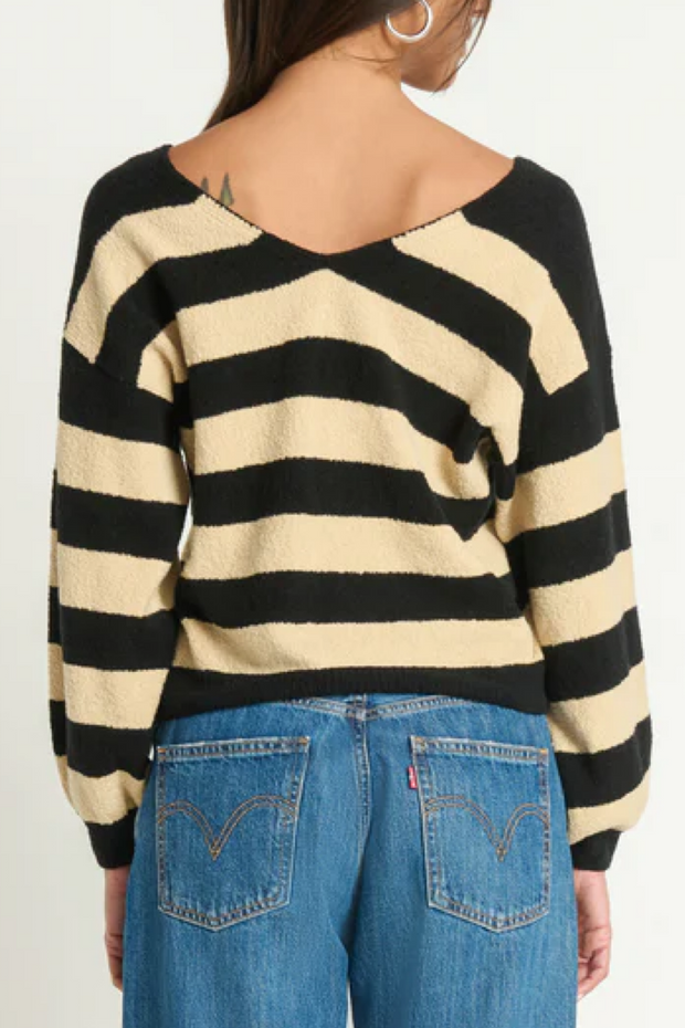 Person wearing a black and beige striped sweater with blue jeans